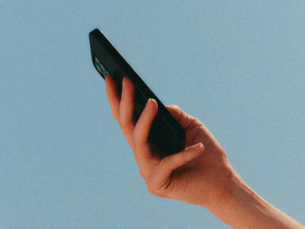 Hand håller upp en mobiltelefon med blå himmel i bakgrunden