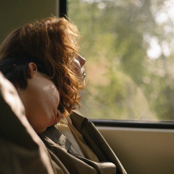 A person looking out the window of a vehicle. Another person is resting on the first persons' shoulder. 