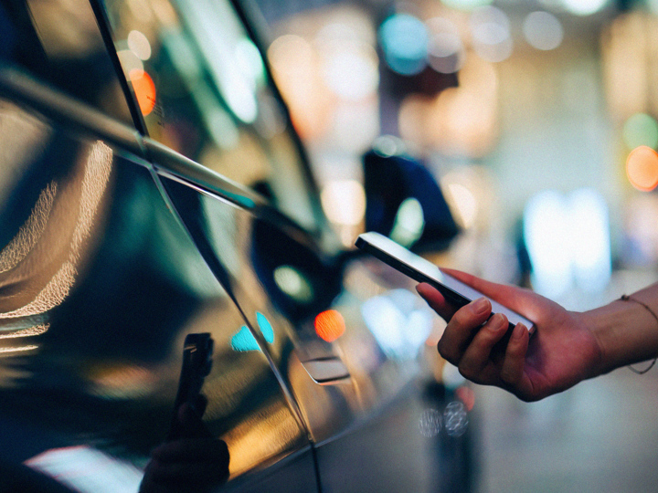 Kvinnlig hand som håller en mobil vid sidan av en bil