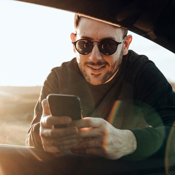 Man som håller i en mobiltelefon samtidigt som han lutar sig på underarmarna in genom fönstret på förarsidan av en bil.