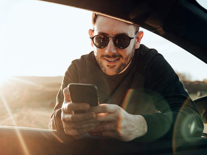 Man som håller i en mobiltelefon samtidigt som han lutar sig på underarmarna in genom fönstret på förarsidan av en bil.