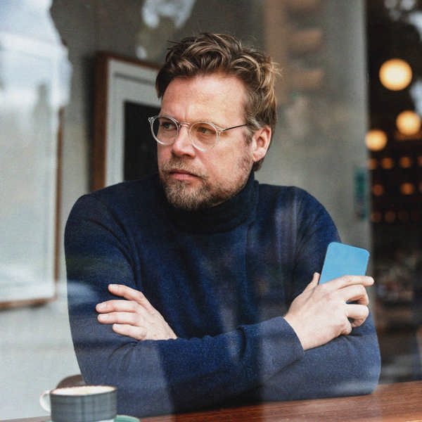 Man med armarna i kors och en mobil i handen på ett café