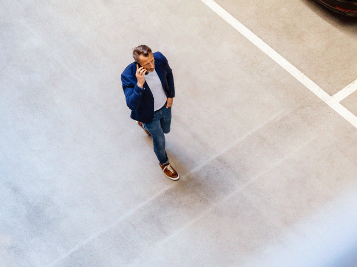 Man som går på en parkeringsplats och pratar i telefon, sedd från ovan.