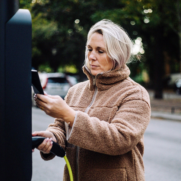 Kvinna som använder sin telefon för att betala vid en laddstation.